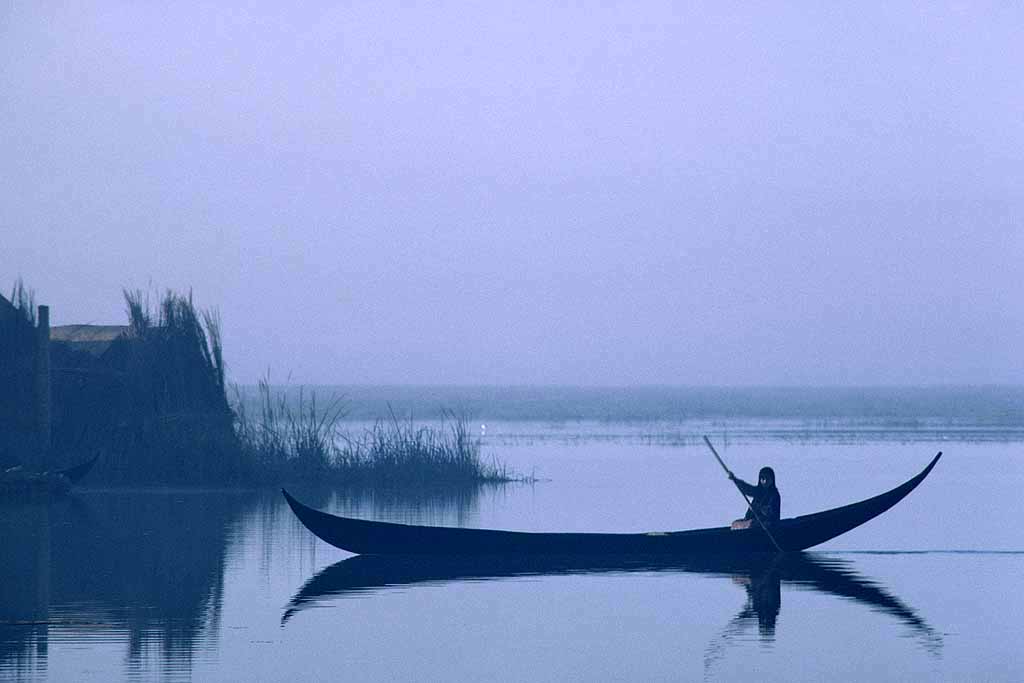 Tor Eigeland - Dream-like image of a woman silently punting her slender canoe pre-dawn in the Central Marshes. W8881